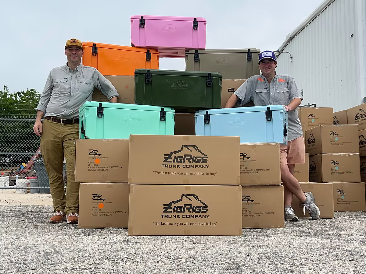 Two men standing next to colorful coolers and boxes with 'ZigRigs Truck Company' branding.